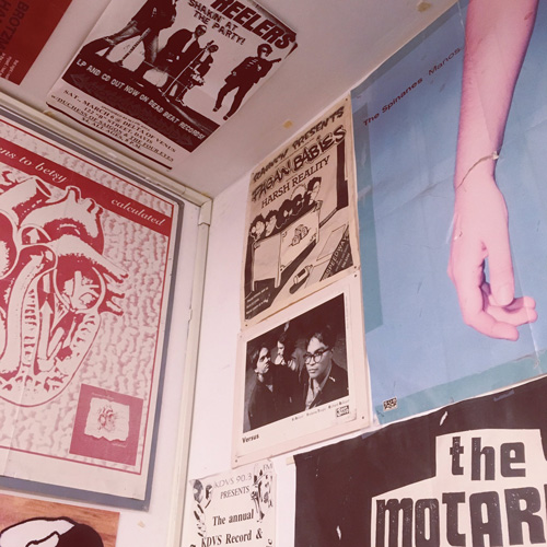 A photo of the corner of a room, near the ceiling, showing posters on the walls and the ceiling.