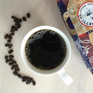 A photo of a cup of black coffee, coffee beans arranged around it in a semi-circle.