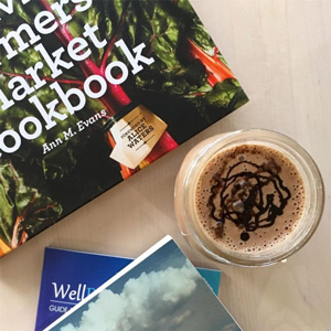 A photo of several books and a smoothie with chocolate drizzle on a table.