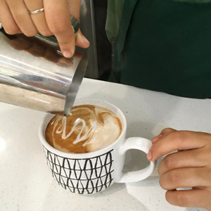 A photo of someone's hands as they pour milk into a latte, creating latte art.